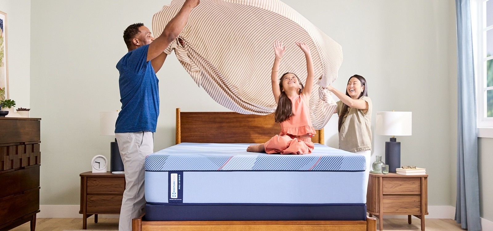 Family laughing as they dress their Posturepedic® Pro Hybrid Tight Top mattress