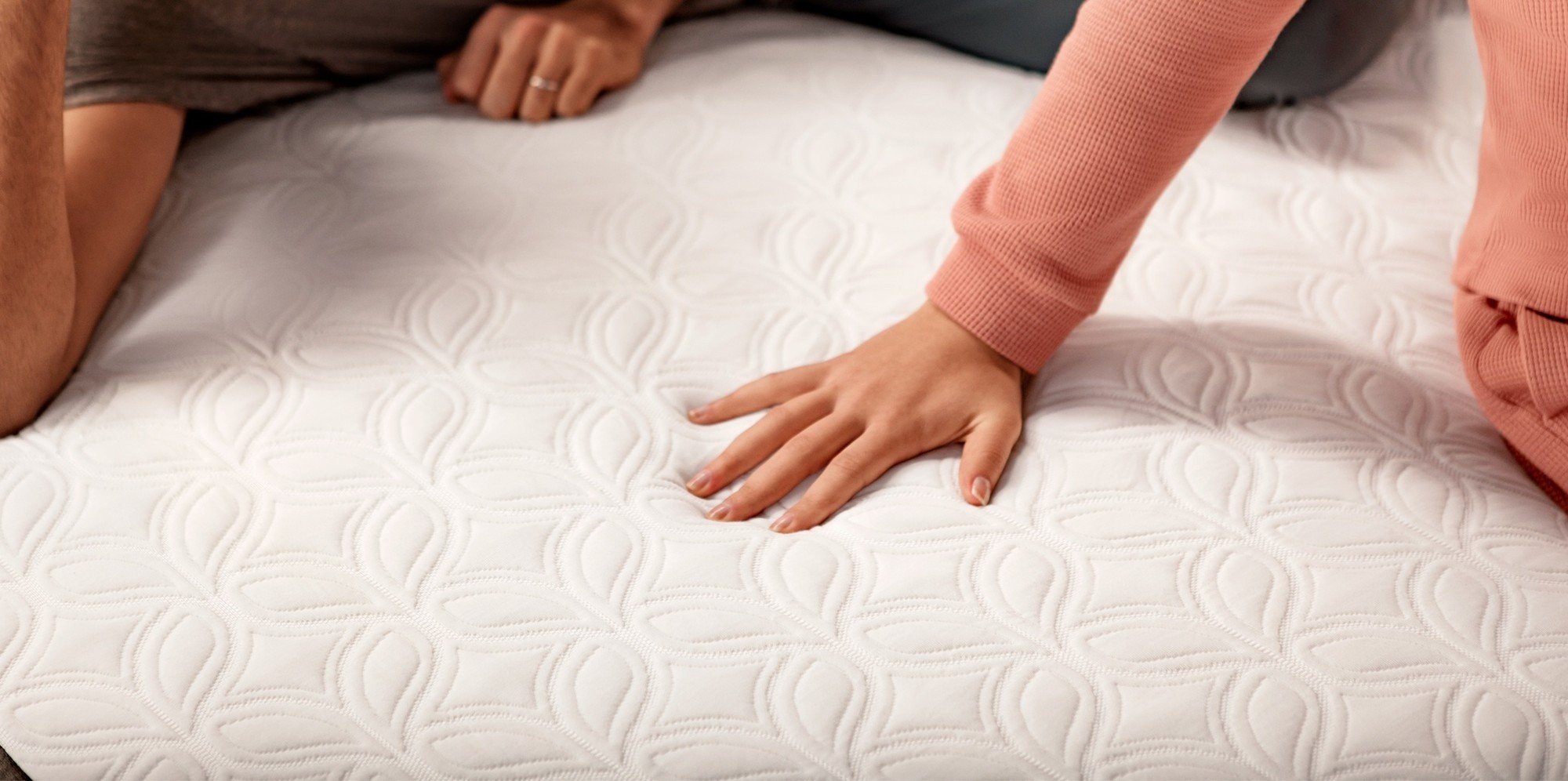 a woman's hand pressing on a chill hybrid mattress and a man laying next to her